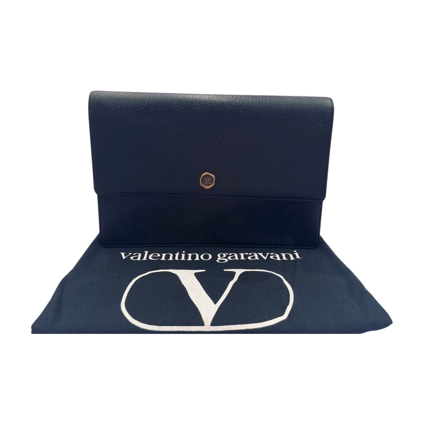 A Valentino Black Leather Clutch from Valentino Garavani is displayed with a snap button closure, positioned on top of an original Valentino dust bag adorned with a large white "V" and the brand name "Valentino Garavani" written in white letters.