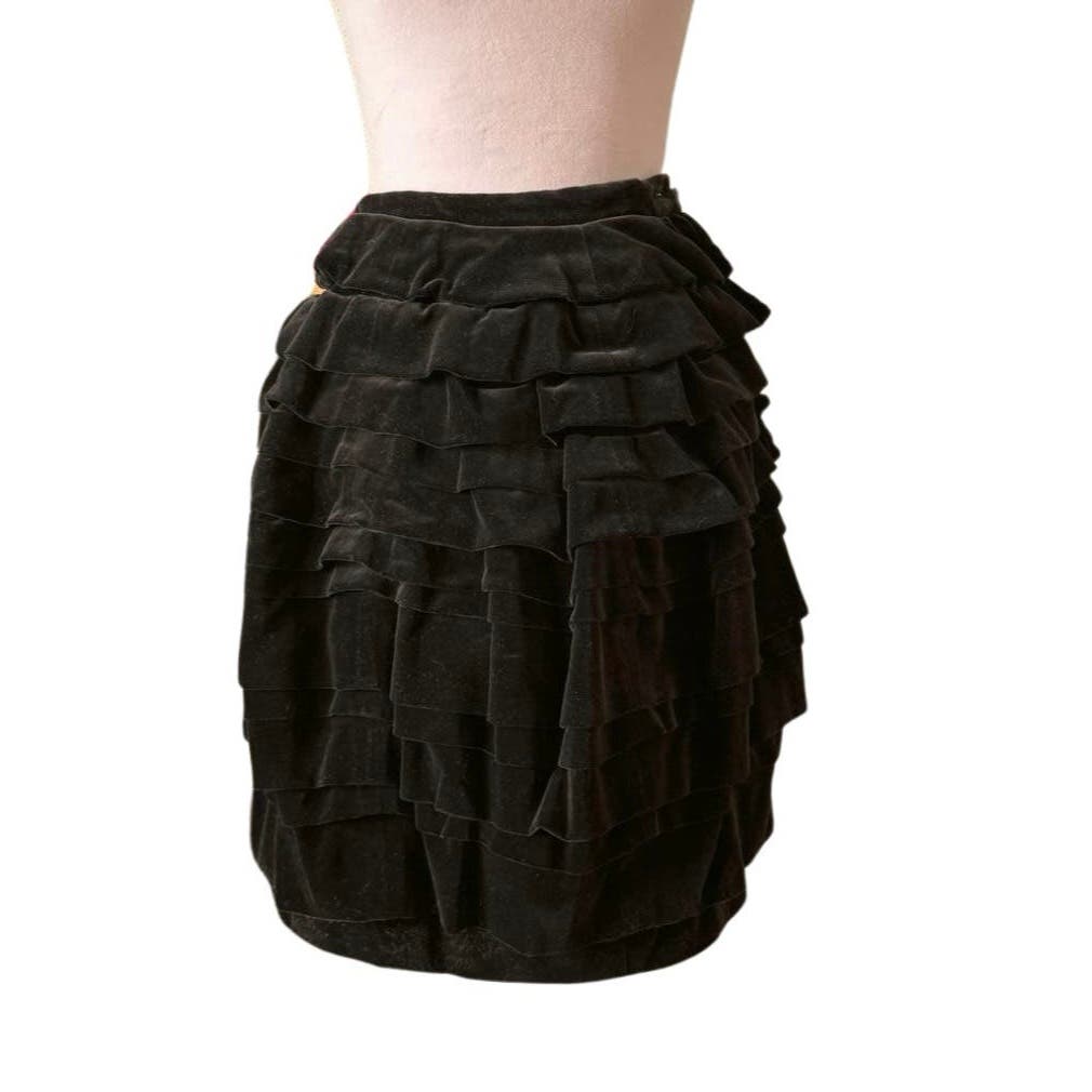 A Vintage 1990 Comme des Garcons Skirt with multiple horizontal ruffles displayed on a dress form. This knee-length piece features a fitted waist and a layered, textured appearance, reminiscent of 90s Comme des Garçons designs. The background is plain and white, highlighting its vintage condition.