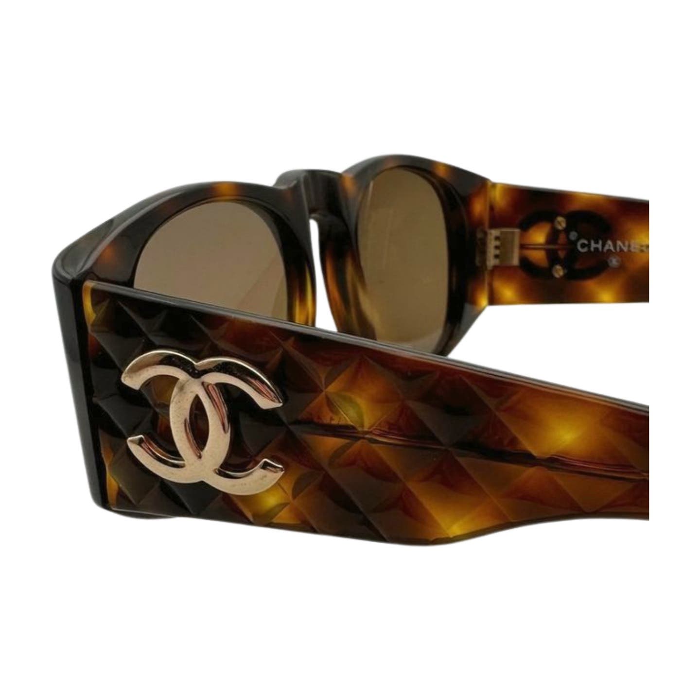 Close-up image of Vintage 90’s Chanel Sunglasses with thick, dark tortoiseshell frames featuring a diamond quilted pattern on the arms and the iconic Chanel logo in metallic gold on the temple. The lenses are tinted brown.