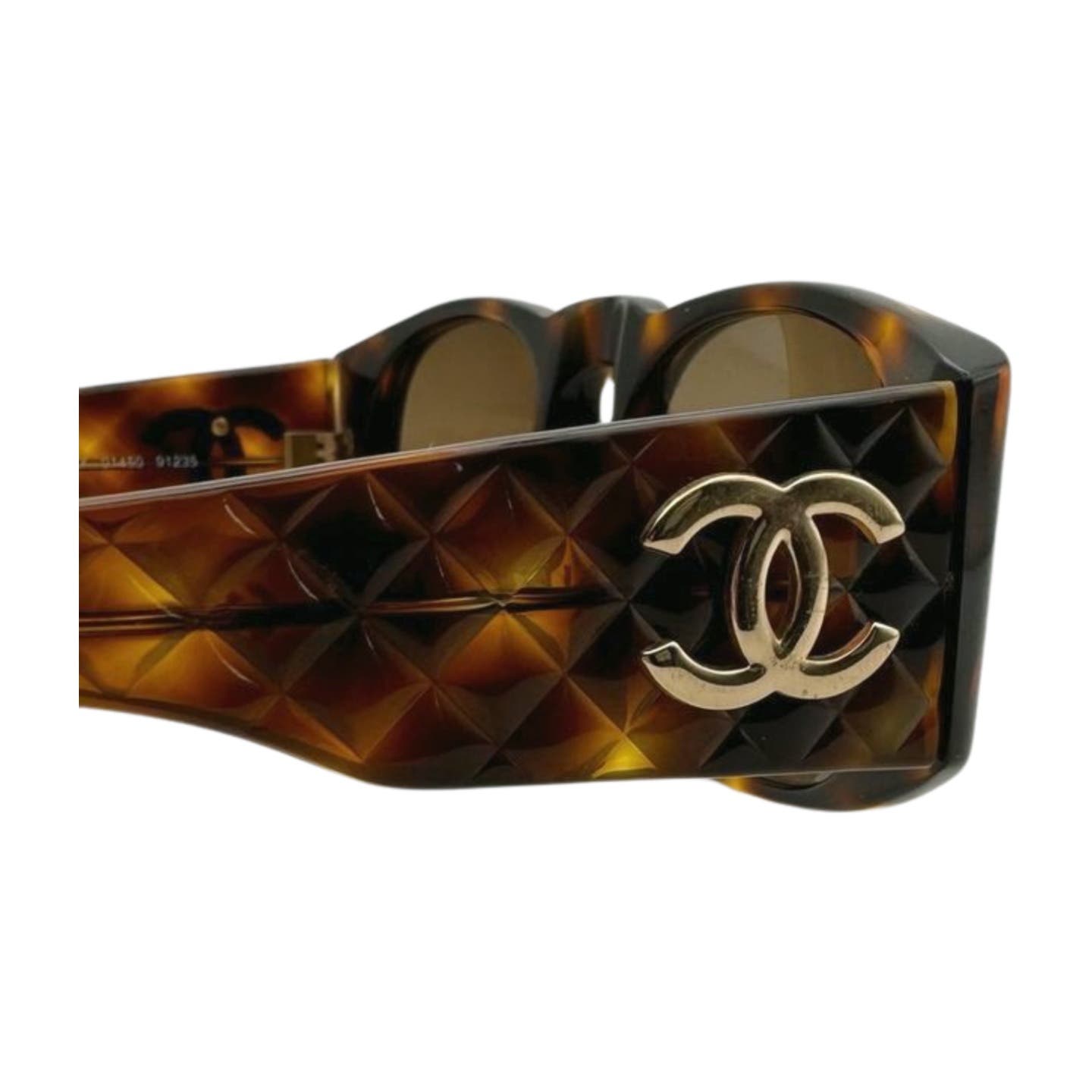 Close-up of the side of a pair of Vintage 90’s Chanel Sunglasses with a brown, tortoise shell textured pattern and gold-toned interlocking "CC" logo. The frame features an embossed design, adding an element of luxury to the eyewear paired with quilted arms for added elegance.