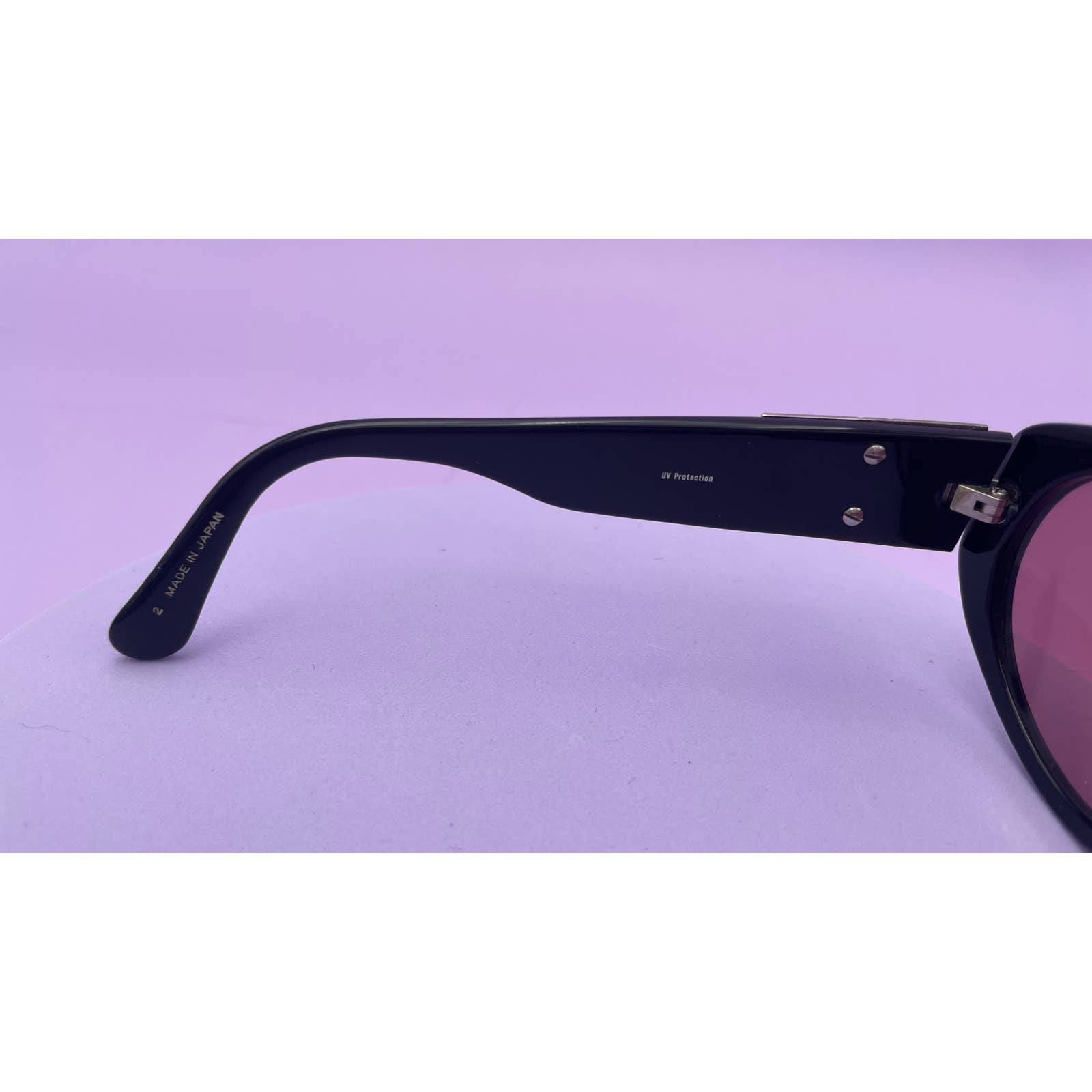A close-up of the stylish side arm of a pair of Saint Laurent YSL Vintage Logo Sunglasses with hinge detailing. The arm, in excellent condition, has "52 Polarized" written on its inner side. The background is a solid light purple color.