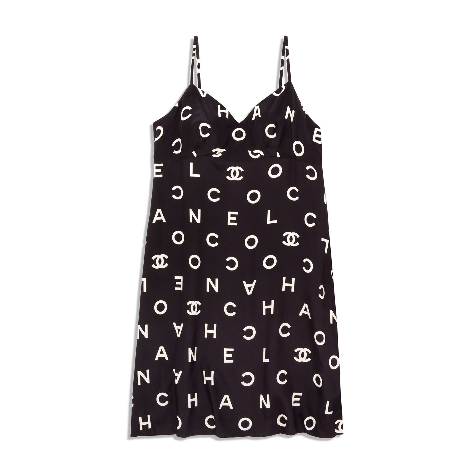 A black sleeveless dress with thin straps, featuring a pattern of white letters spelling "CHANEL" and the Chanel logo scattered across the fabric. This Vintage Chanel 1997 Runway Alpha Logo Coco Print Slip Dress and Jacket Set from Chanel has a V-neckline and a straight silhouette that reaches just above the knees.